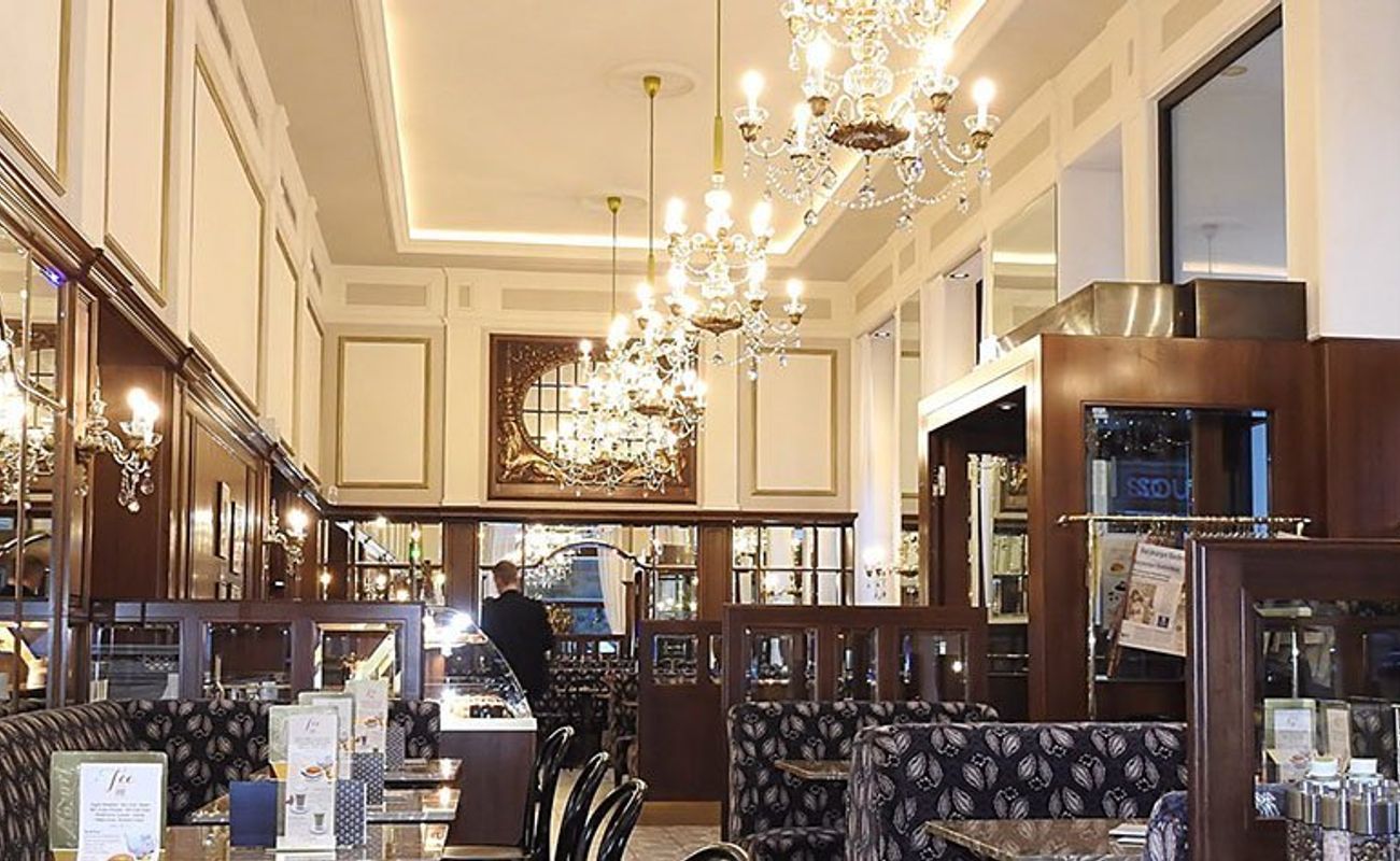 Elegantes Restaurant mit Kronleuchtern, Spiegeln und stilvollen Möbeln. Tische sind gedeckt, Atmosphäre ist luxuriös und einladend.